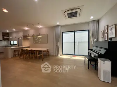 Spacious open-plan living room with dining area and piano, featuring modern lighting and large windows.