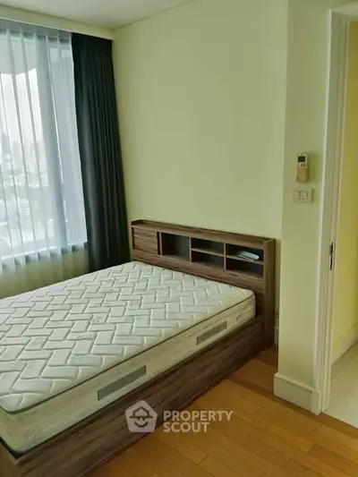 Cozy bedroom with wooden flooring and large window offering city views, featuring a modern bed frame and mattress.