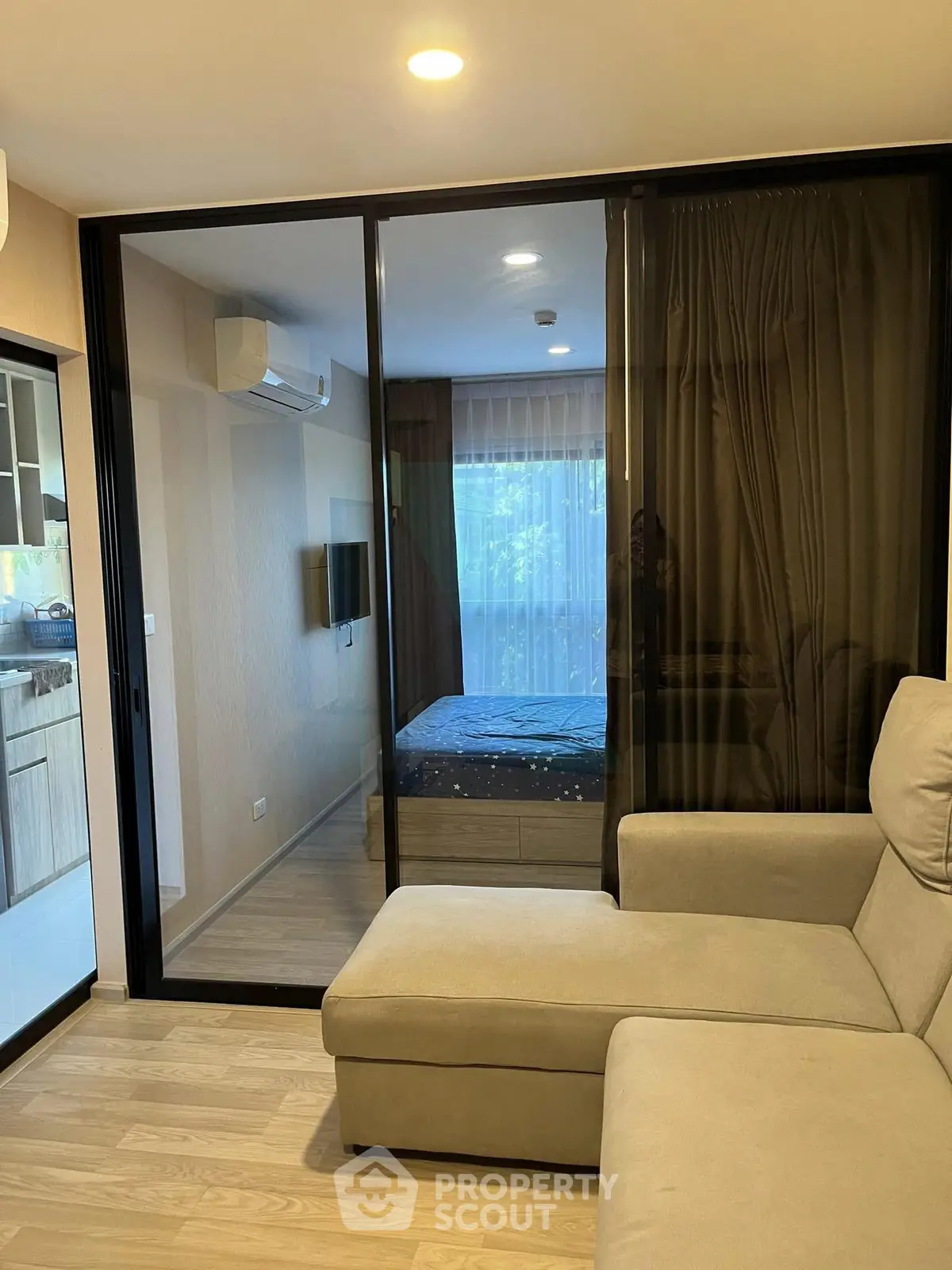 Modern apartment interior with glass partition separating living room and bedroom, featuring cozy furniture and natural light.