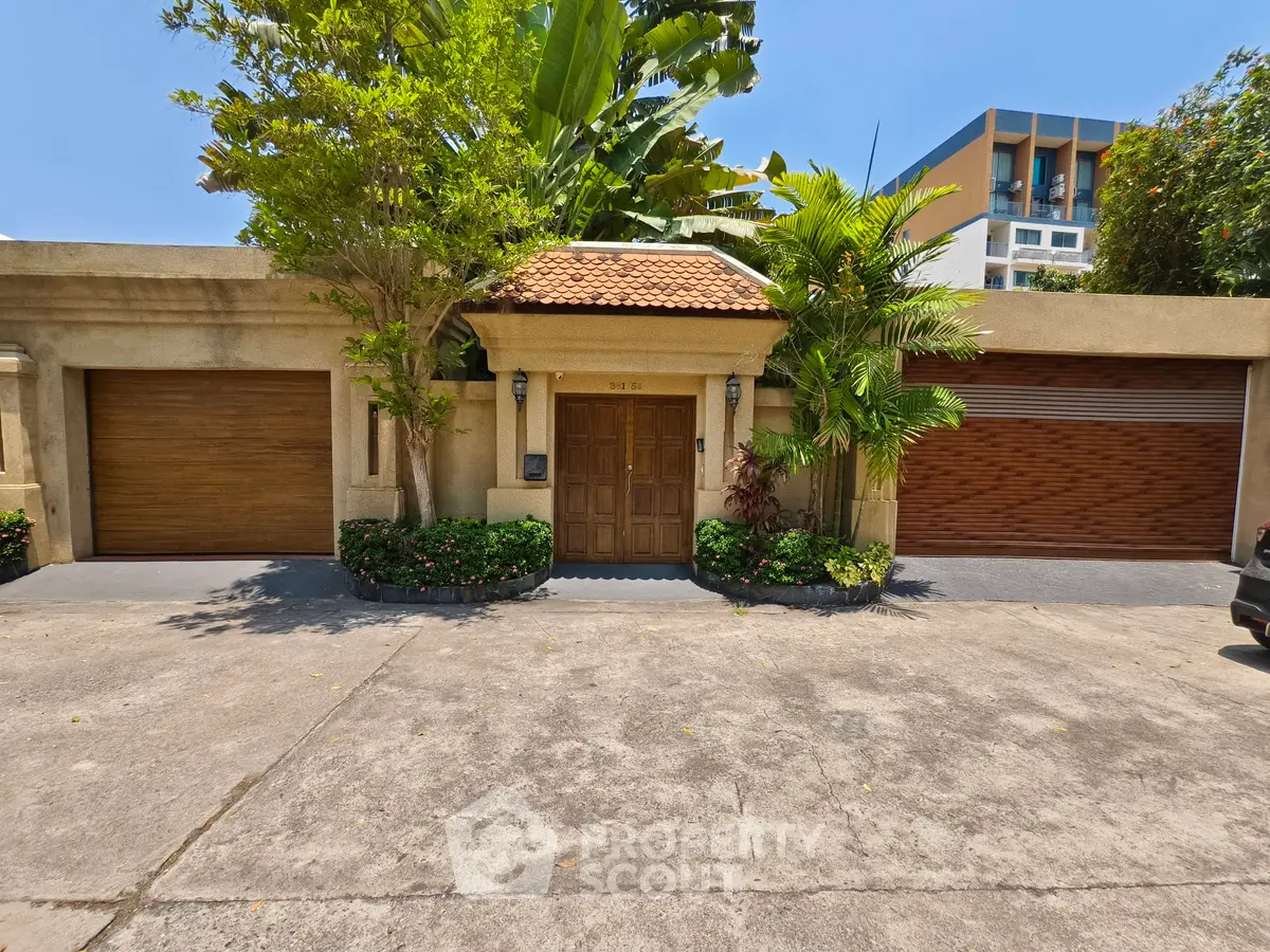Charming villa entrance with lush greenery and modern garage doors in a serene neighborhood.