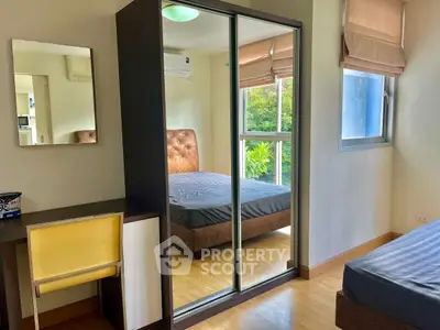 Modern bedroom with mirrored wardrobe and desk, featuring natural light and stylish decor.