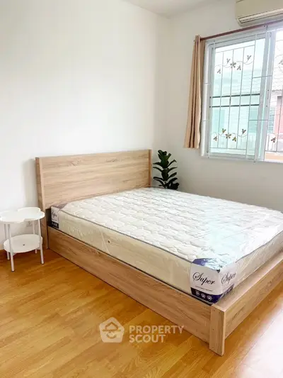 Cozy bedroom with wooden flooring and large window for natural light