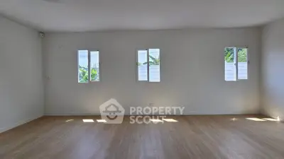 Spacious empty room with wooden flooring and natural light from three windows.