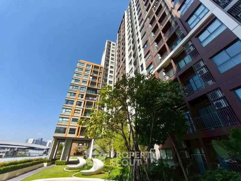Modern high-rise apartment building with lush green garden and clear blue sky.
