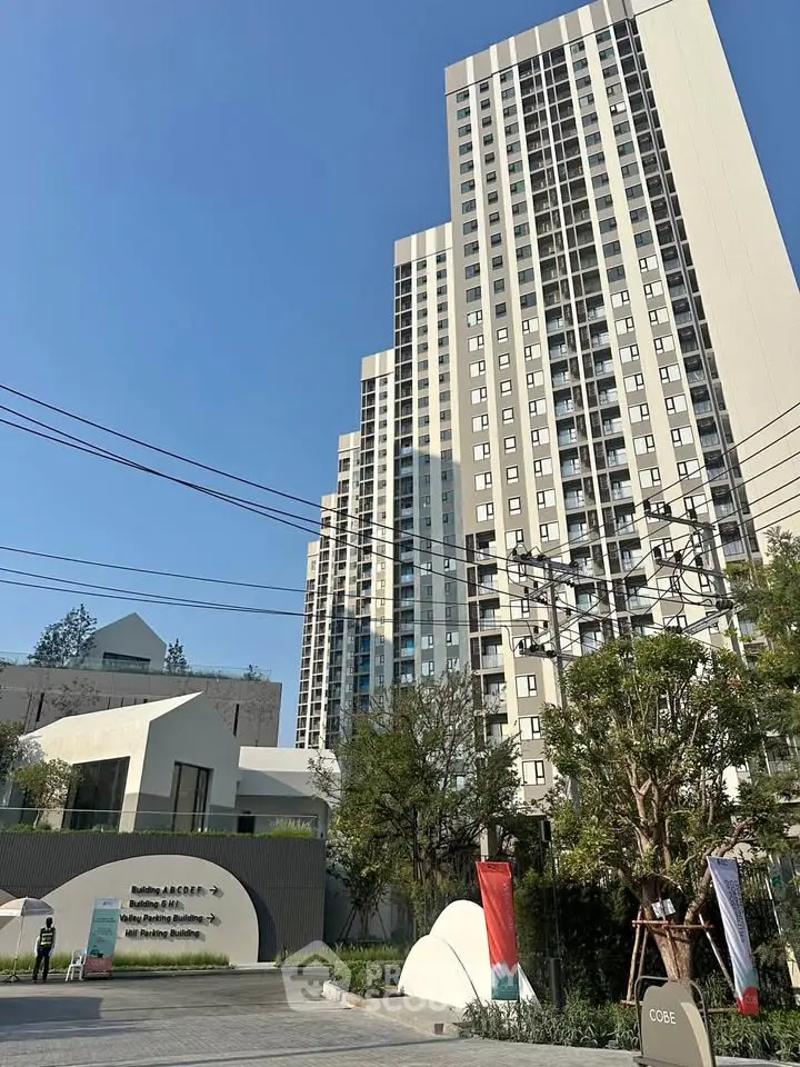 Modern high-rise residential building with lush greenery and clear blue sky.