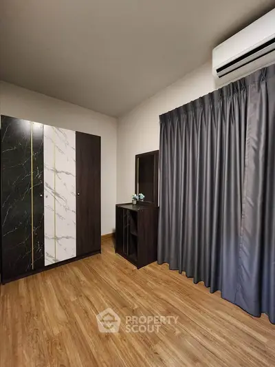 Modern bedroom with stylish wardrobe and air conditioning, featuring elegant wooden flooring and dark curtains.