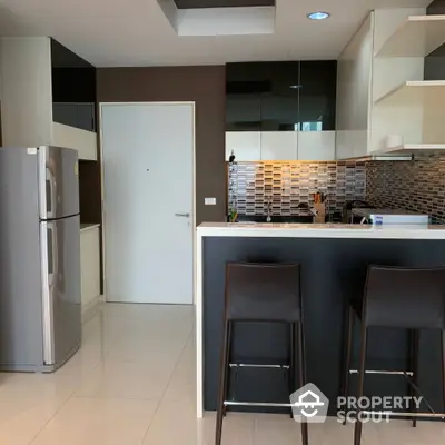 Modern kitchen with sleek design, bar seating, and stainless steel appliances in a stylish apartment.