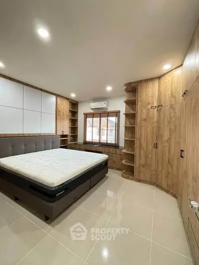Spacious modern bedroom with built-in wooden storage and large window for natural light.
