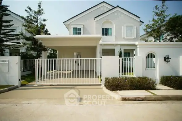 Charming white two-story house with gated driveway and lush greenery, perfect for family living.