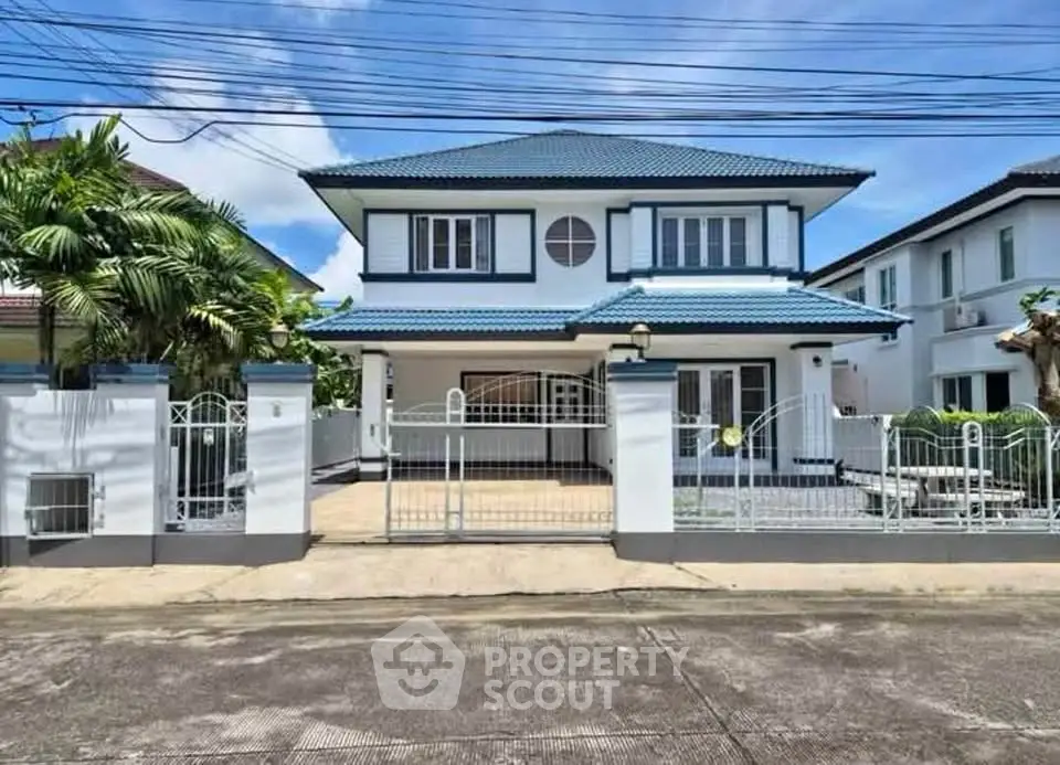 Charming two-story house with blue roof and gated entrance in a serene neighborhood.