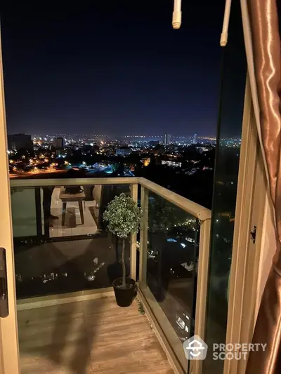 Stunning night city view from a modern balcony with glass railing and potted plant.