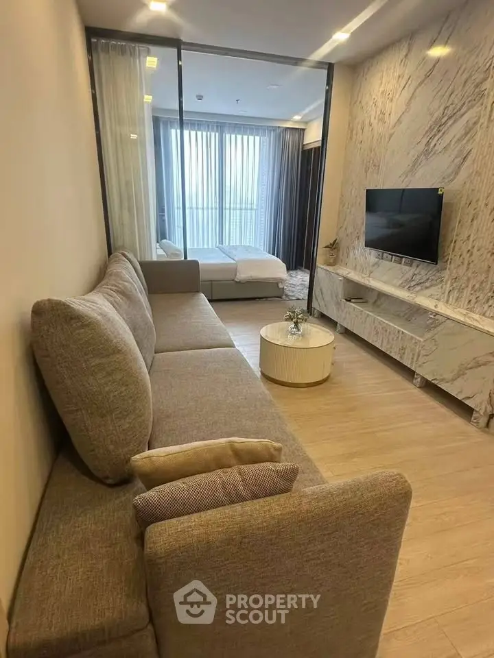 Modern living room with stylish sofa and TV, featuring a cozy bedroom view through glass partition.