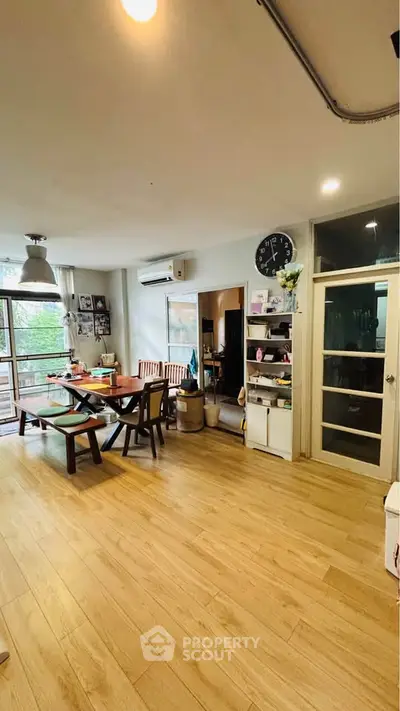 Spacious living room with wooden flooring and modern decor, featuring a dining area and large windows.