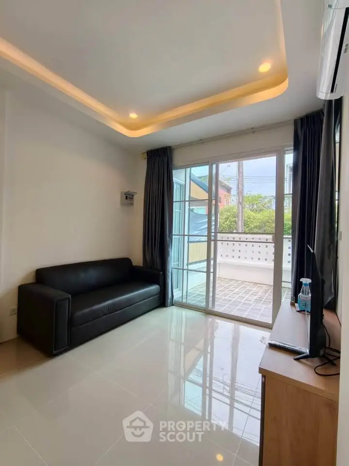 Modern living room with sleek black sofa and large glass doors leading to a balcony.