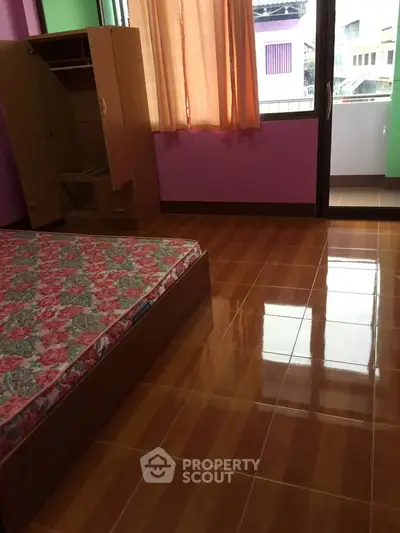 Cozy bedroom with vibrant walls and balcony access, featuring a floral mattress and wooden wardrobe.