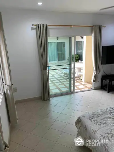 Spacious bedroom with sliding glass doors leading to a tiled balcony, offering a seamless indoor-outdoor living experience.