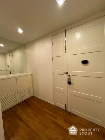 Spacious entryway with wooden flooring and mirrored wall in modern apartment.