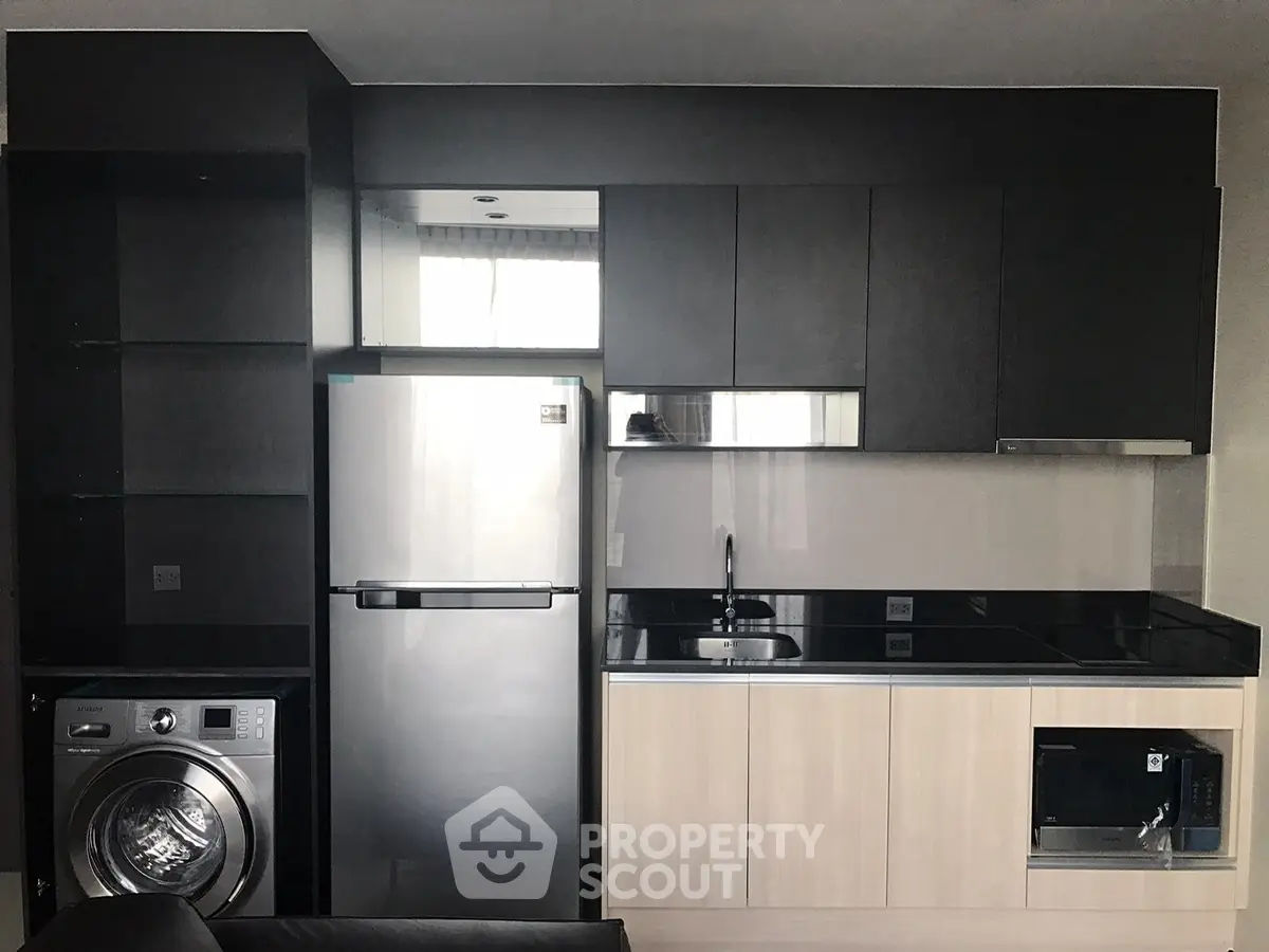 Modern kitchen with sleek cabinets, stainless steel fridge, and washing machine.
