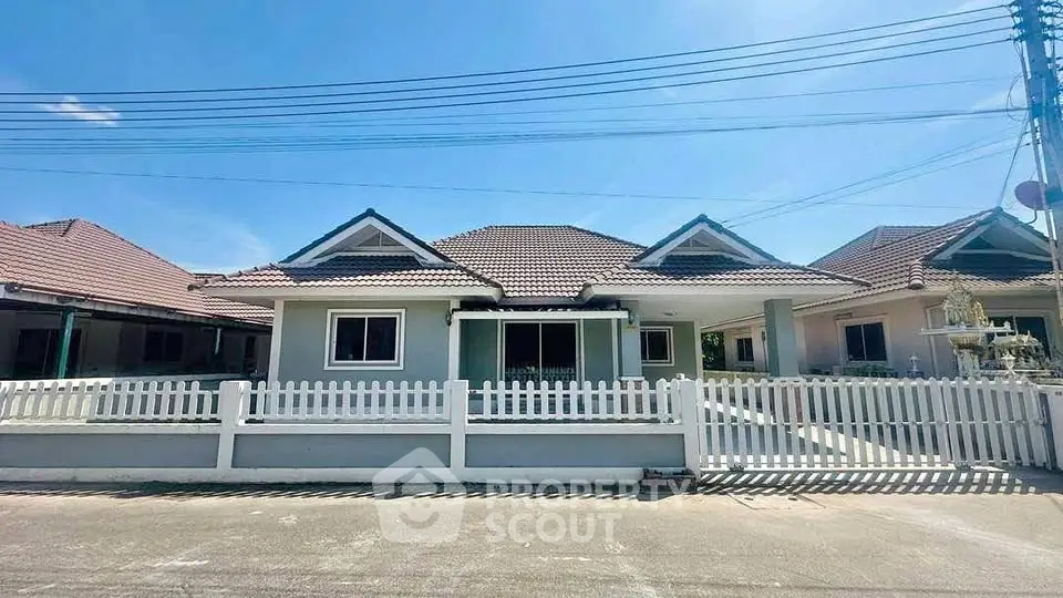 Charming suburban house with white picket fence and tiled roof under clear blue sky.