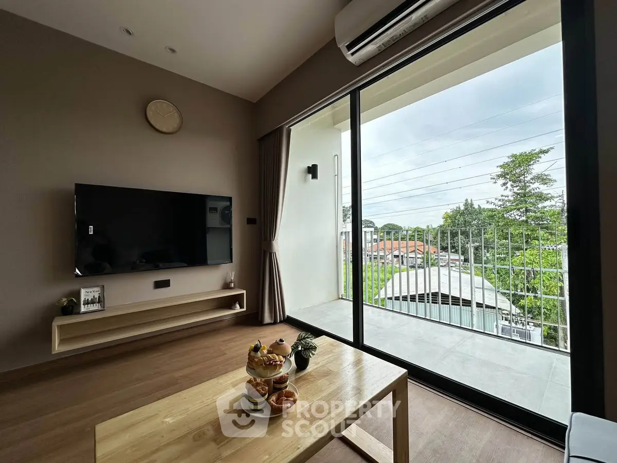 Modern living room with large balcony and scenic view, featuring sleek TV setup and cozy decor.