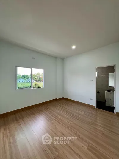 Spacious empty room with wooden flooring and large window, ideal for customization.