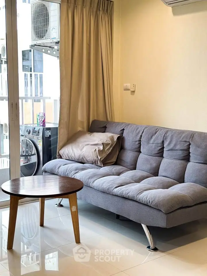 Cozy living room with modern gray sofa and round wooden coffee table near large window.