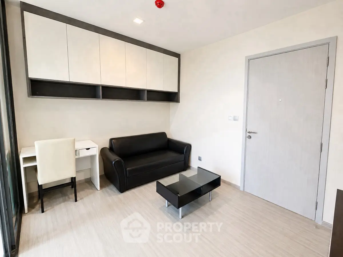 Modern living room with sleek black sofa, glass coffee table, and built-in storage cabinets.