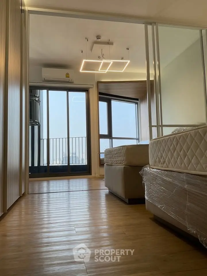 Modern bedroom with large windows and balcony access, featuring sleek wooden flooring and contemporary lighting.