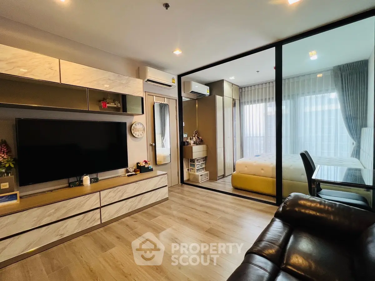 Modern living room with open layout and glass partition to bedroom, featuring sleek furniture and ambient lighting.