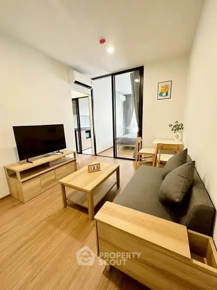 Modern living room with wooden furniture and TV, open to bedroom view.