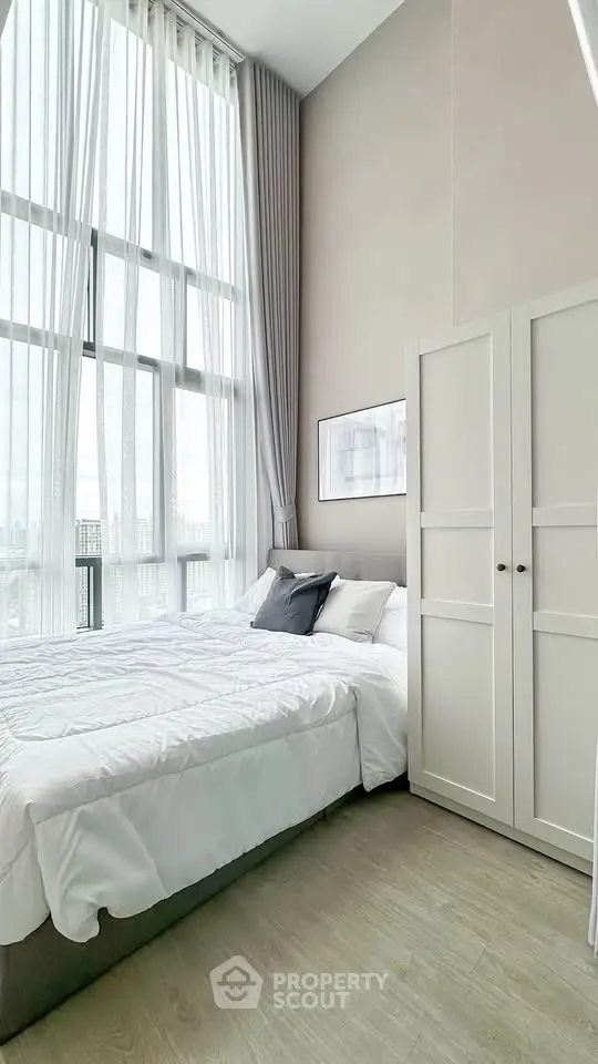 Spacious bedroom with high ceilings and large windows offering natural light and city views.