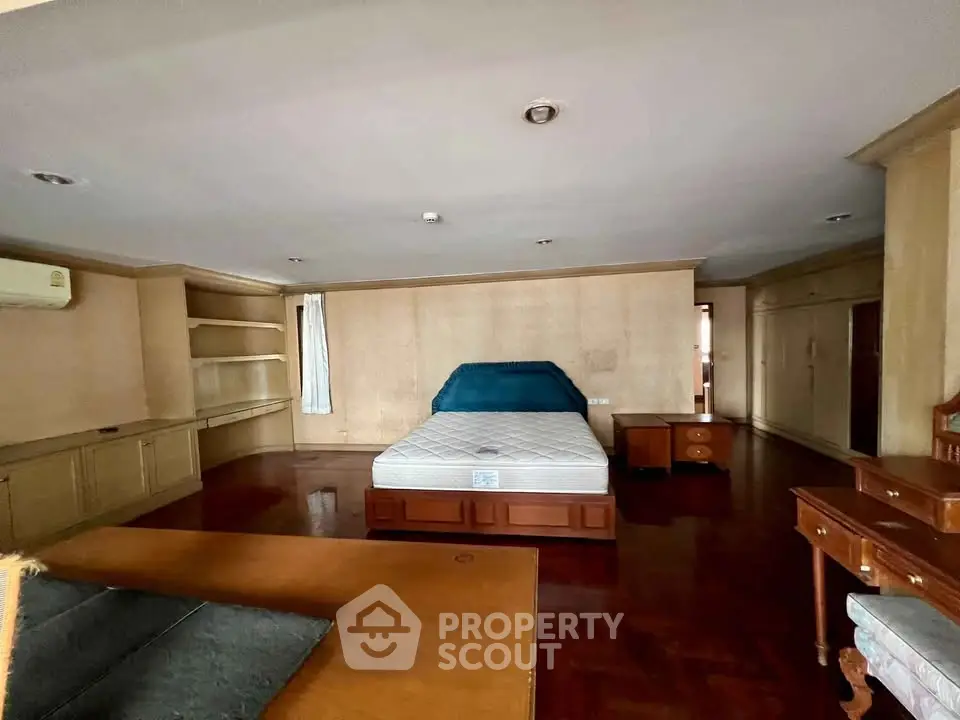 Spacious bedroom with wooden flooring and built-in shelves, featuring a large bed and ample natural light.