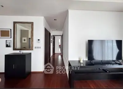 Modern living room with sleek furniture and wooden flooring, featuring a large TV and elegant decor.