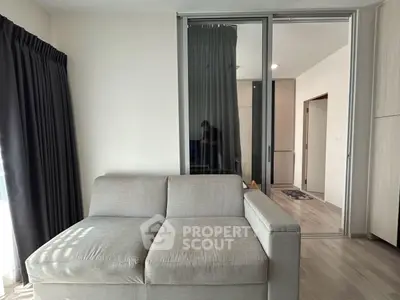 Modern living room with sleek gray sofa and sliding glass doors leading to a cozy bedroom.