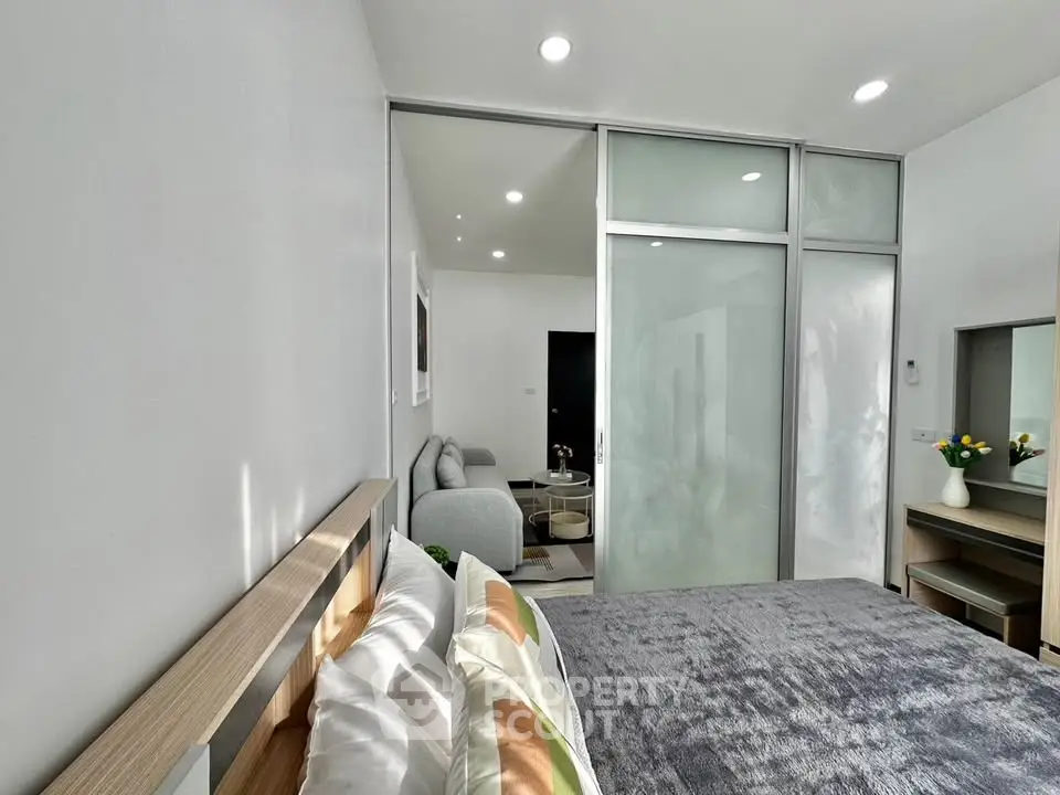 Modern bedroom with sliding glass doors and cozy living area, featuring stylish decor and ample natural light.