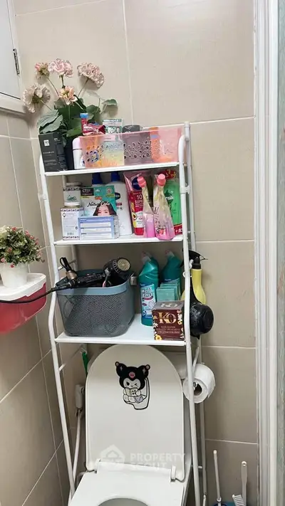 Compact bathroom with organized storage shelves above toilet, featuring cleaning supplies and decor.