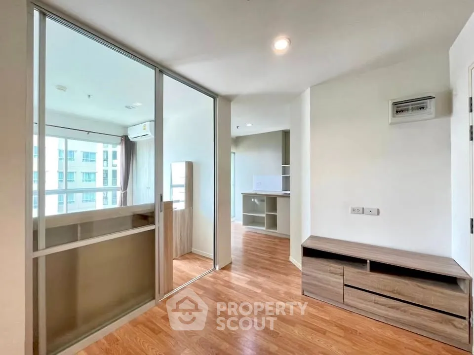 Modern apartment interior with wooden flooring and glass partition, featuring built-in storage and natural light.