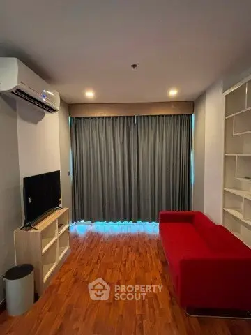 Modern living room with red sofa, TV, and air conditioning, featuring wooden flooring and stylish shelving.