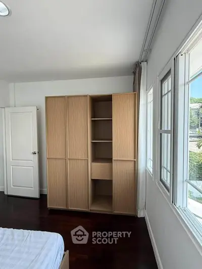 Spacious bedroom with large windows and wooden wardrobe, offering ample natural light and storage.