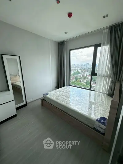 Modern bedroom with large window offering stunning city view, featuring sleek furnishings and natural light.