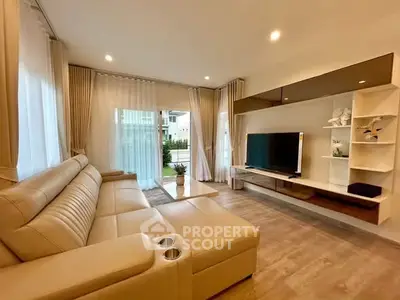 Modern living room with beige leather sofa and large TV, featuring elegant decor and natural light.