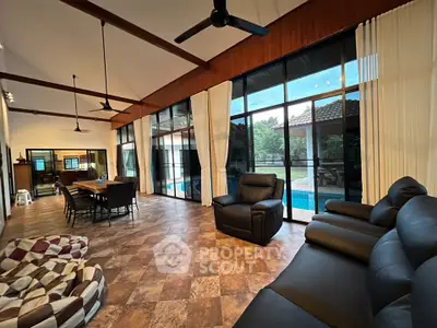 Spacious living room with high ceilings and pool view, featuring modern furniture and large windows.