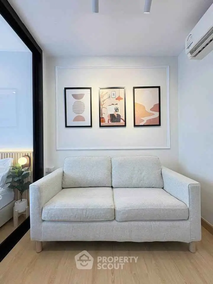 Modern living room with cozy sofa and stylish wall art, featuring a glimpse of a bedroom through glass partition.