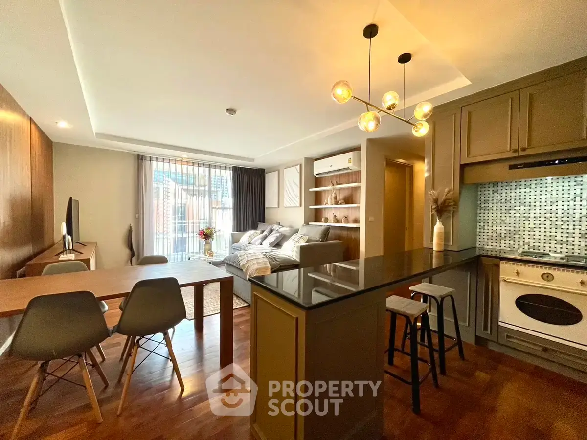 Modern open-plan living room with stylish kitchen and cozy dining area, featuring elegant lighting and hardwood floors.