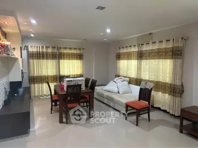 Spacious living room with dining area and modern decor, featuring large windows and elegant curtains.