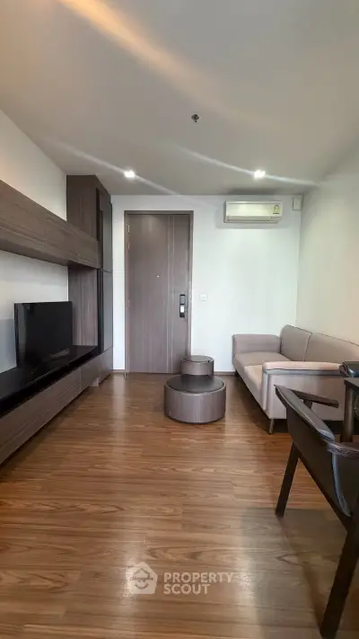 Modern living room with sleek wooden flooring and contemporary furniture, featuring a cozy sofa and entertainment unit.