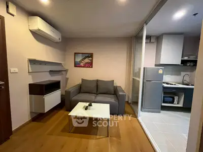 Modern compact living room with kitchen, featuring sleek furniture and wooden flooring.