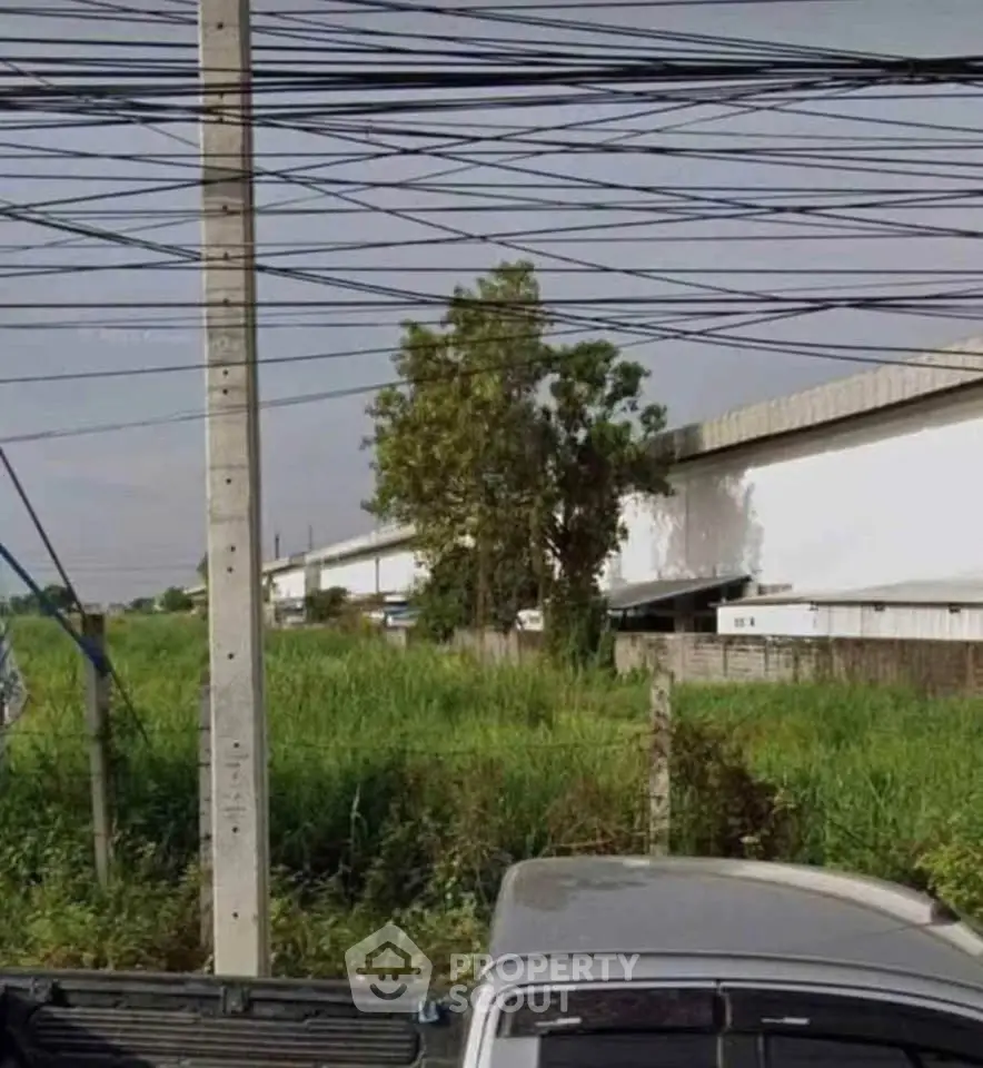 Industrial warehouse exterior with surrounding greenery and power lines.