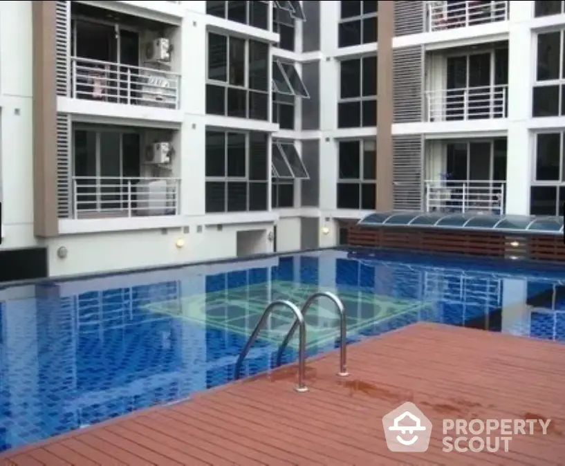 Inviting residential complex pool with wooden deck and modern building facade, perfect for leisure and social gatherings.