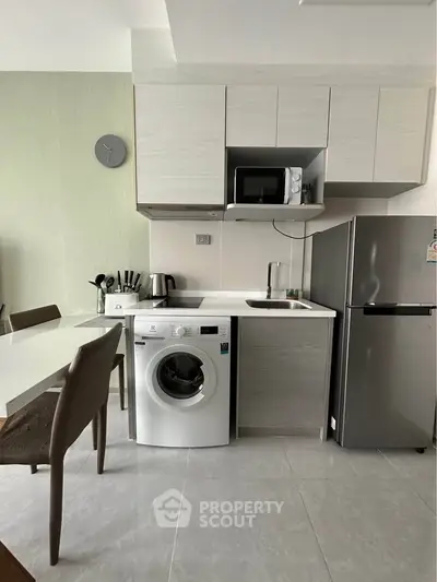 Modern kitchen with washing machine, microwave, and fridge in compact layout.